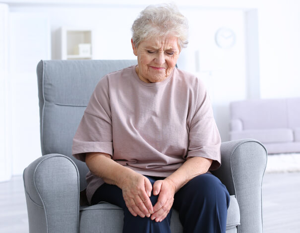 Femme âgée assise sur un sofa, tenant son genoux en raison de la douleur