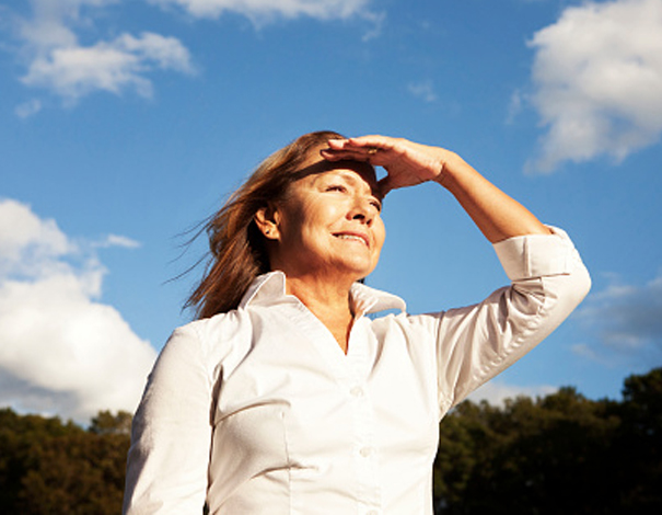 Woman staring out into a field shielding her eyes from the sun