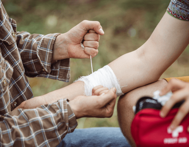 Someone putting a bandage on a person's hurt arm using a first aid kit