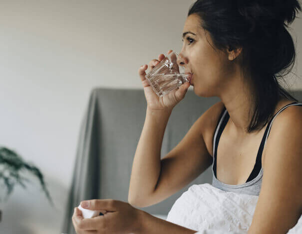 Jeune femme prenant un médicament et buvant un verre d'eau