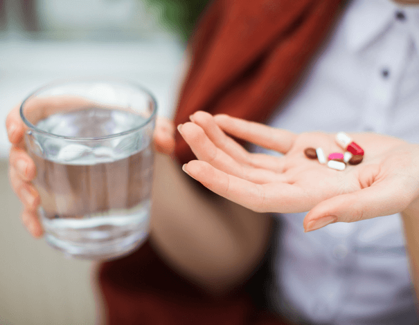 Main de femme tenant des médicaments et un verre d'eau